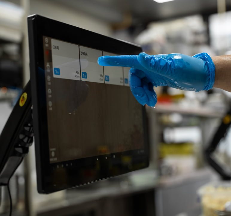 A hand in a blue nitrile glove tapping order tickets on the screen