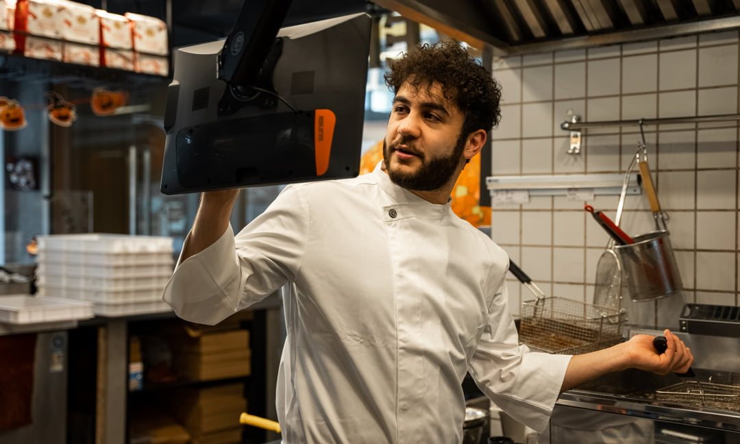 A chef reaching up to an overhead kitchen display in a tiled kitchen