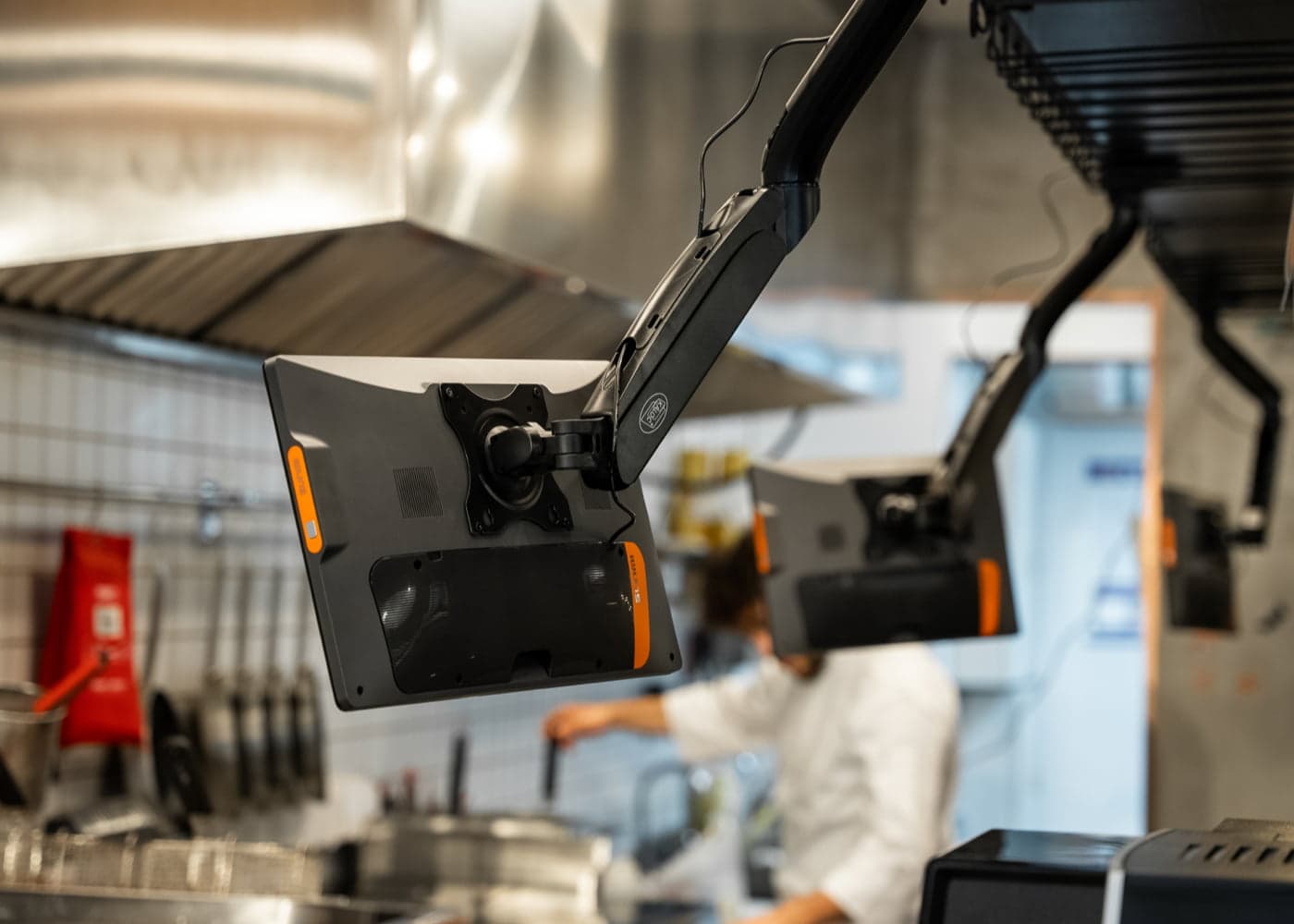Kitchen displays on black overhead arms above a kitchen line, a chef working below them
