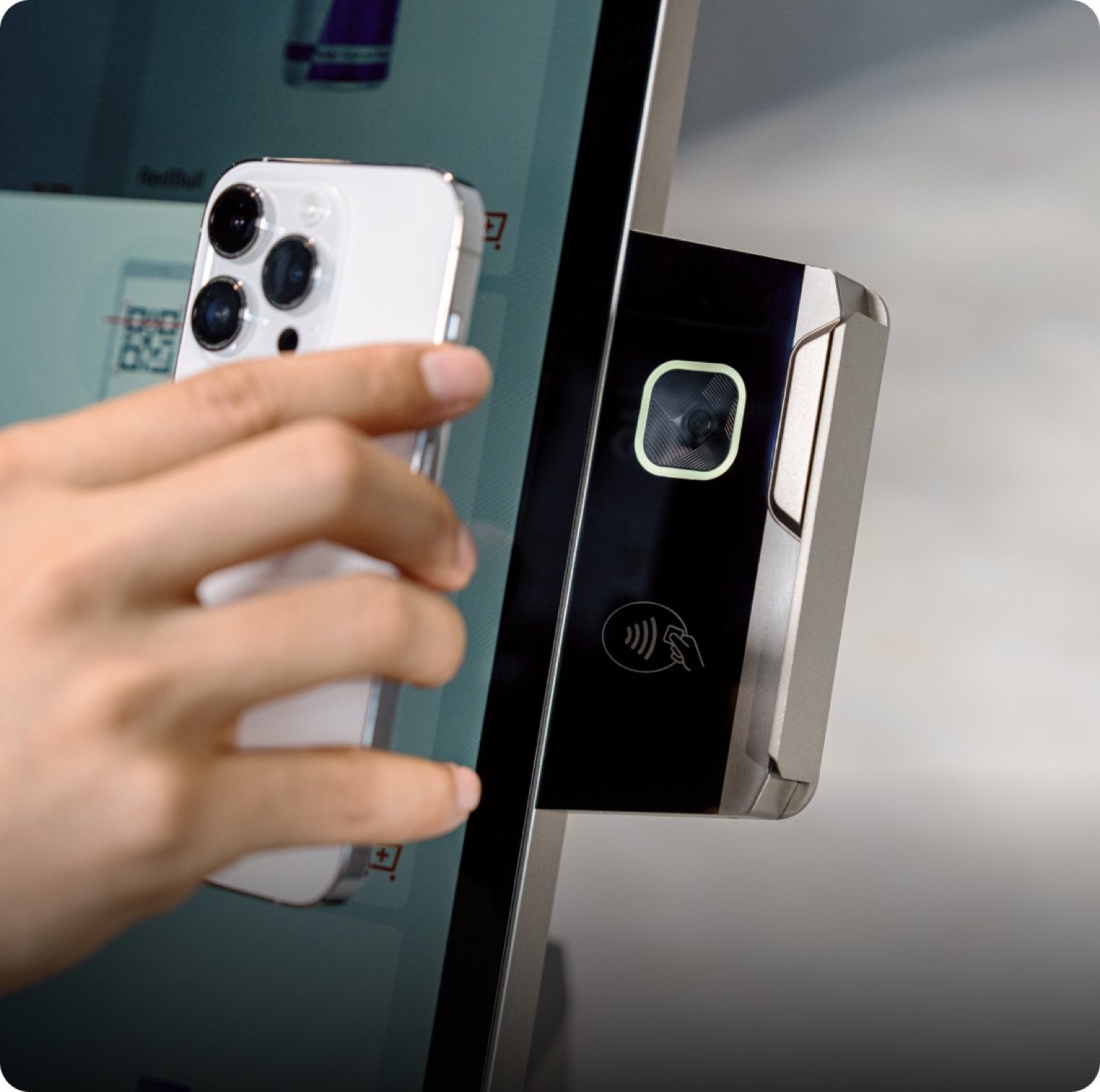 A phone held to the reader module on the side of a kiosk, a QR code on the screen behind it