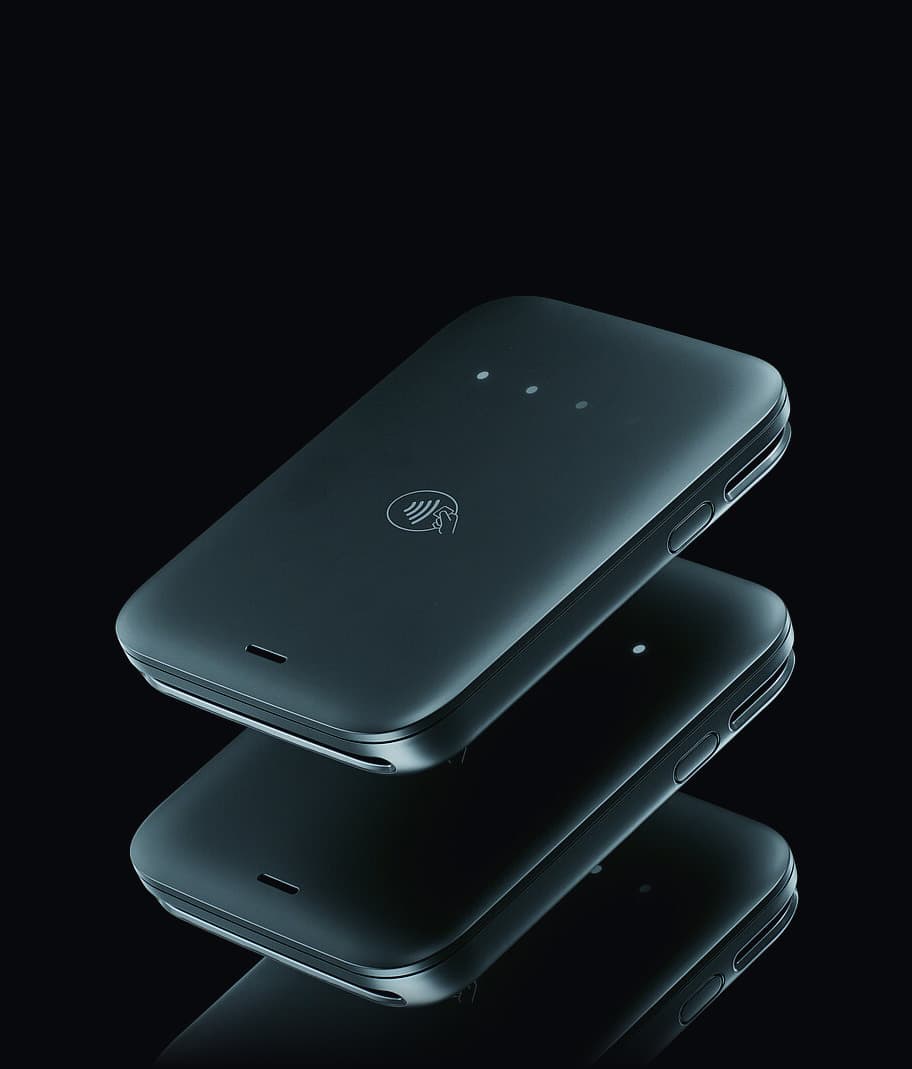 The Final Move reader seen from above at an angle, floating over its own reflection on a black surface, the contactless mark and the status lights visible on its face