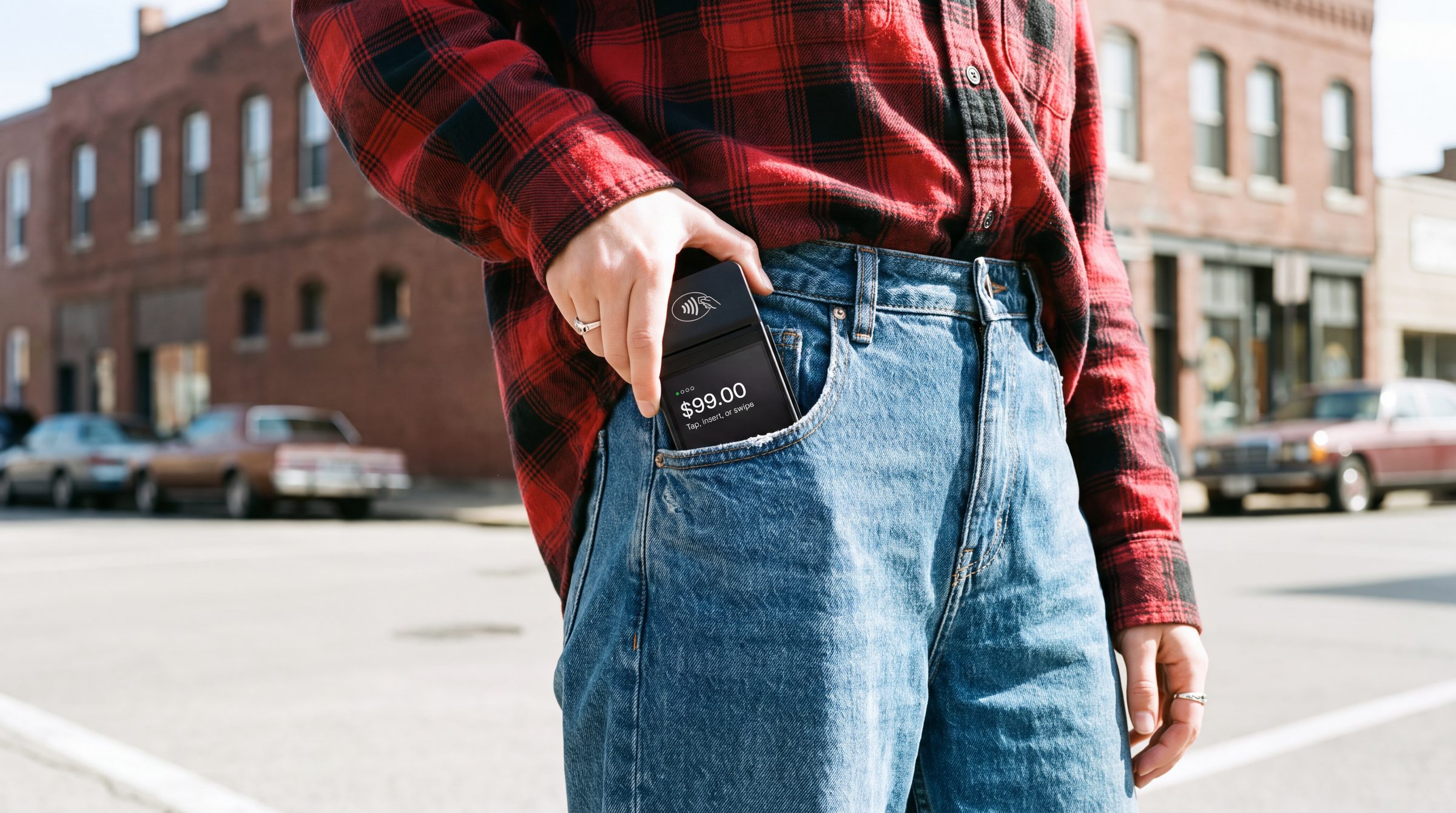 A hand slipping the terminal into a jeans pocket on a street corner, the amount lit on its screen