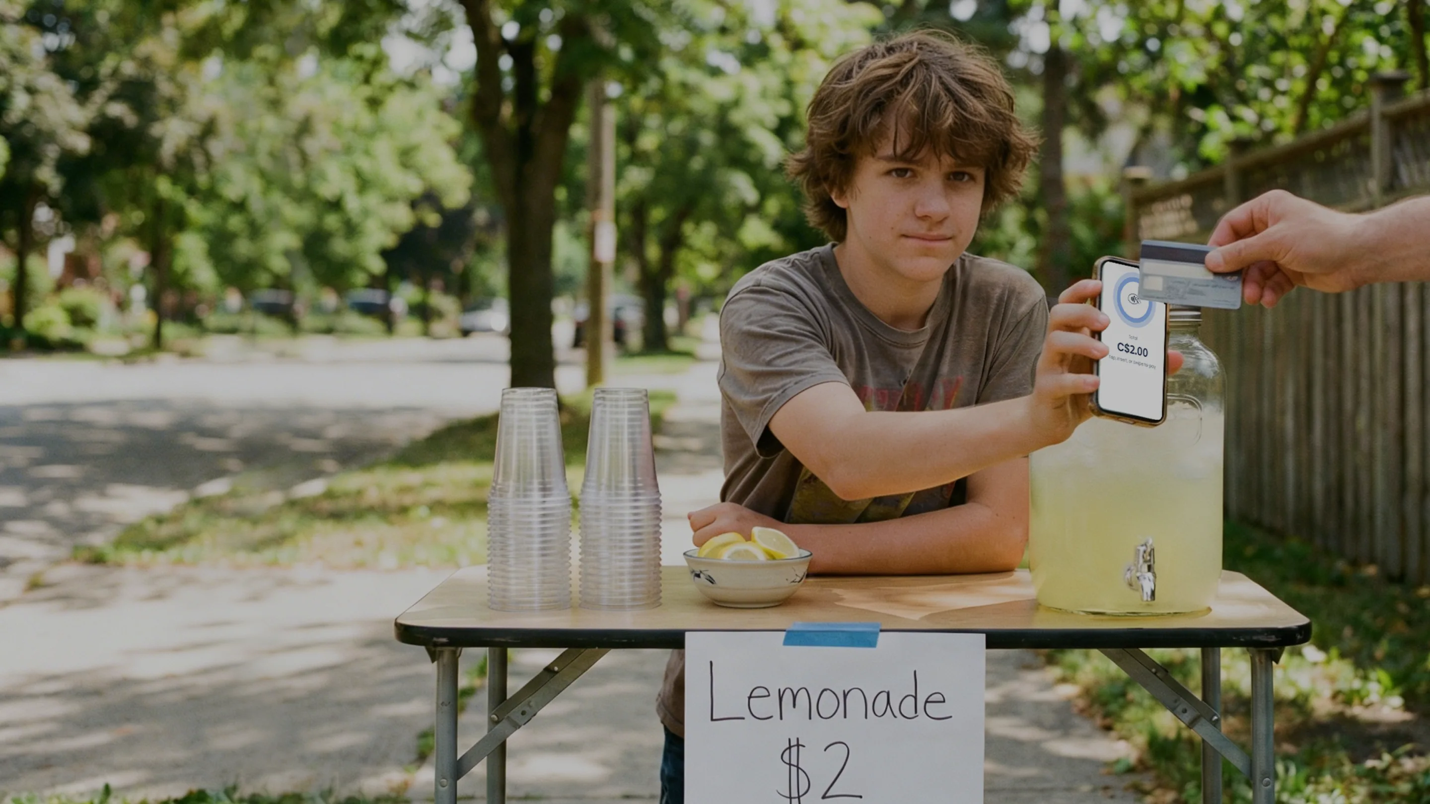 Un adolescente aceptando un pago sin contacto en un puesto de limonada usando Final en un lector de tarjetas